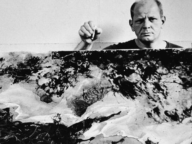 American abstract expressionist painter Jackson Pollock (1912 - 1956) holds a cigarette above and behind one of his paintings in his studio at 'The Springs,' East Hampton, New York, August 23, 1953. (Photo by Tony Vaccaro/Getty Images)